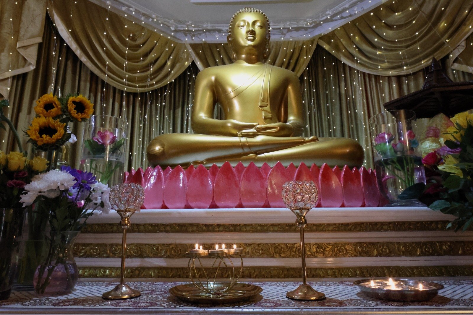 The Vihara's shrine room altar, the Buddha statue framed by golden drapes and lit candles